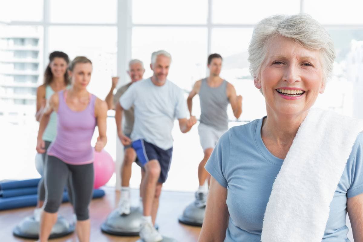 portrait of a cheerful senior woman with people exercising in the background at fitness studio